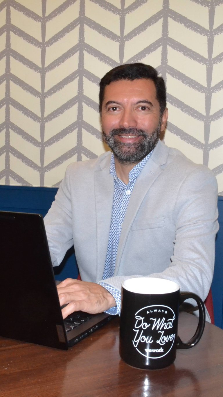 Man in light blazer working at desk with laptop and motivational mug, geometric patterned wallpaper background